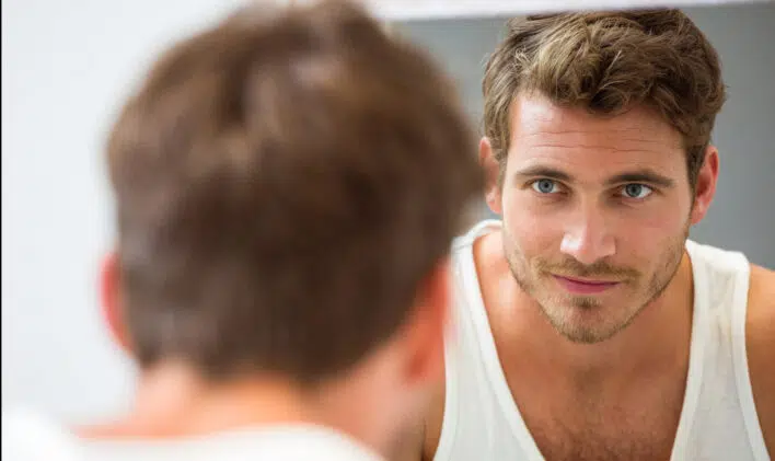 Smart young man looking at himself in mirror at bathroom